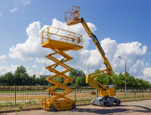 Yellow self propelled articulated boom lift and scissor lift on background of street with trees and sky